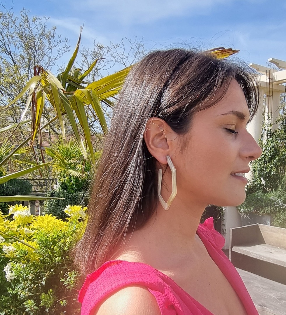 Image d’une femme souriante portant des boucles d’oreilles hexagonales en corne, ajoutant une touche unique et élégante à son look. Parfait pour les accessoires de mode tendance.