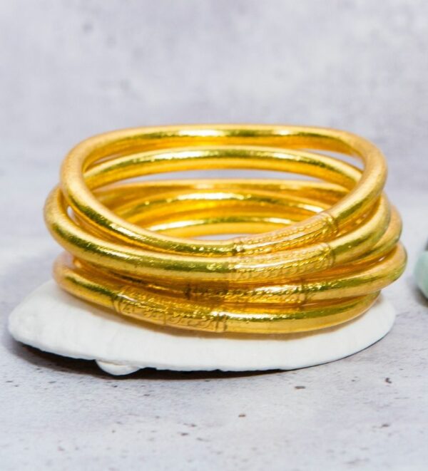 Bracelet-mantra-or Bracelet en or, composé de plusieurs anneaux dorés brillants empilés les uns sur les autres, posés sur une surface blanche