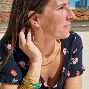 Image d’une femme portant des créoles en corne et plusieurs bracelets joncs dorés et colorés, ajoutant une touche élégante et sophistiquée à son look. Parfait pour les accessoires de mode tendance.