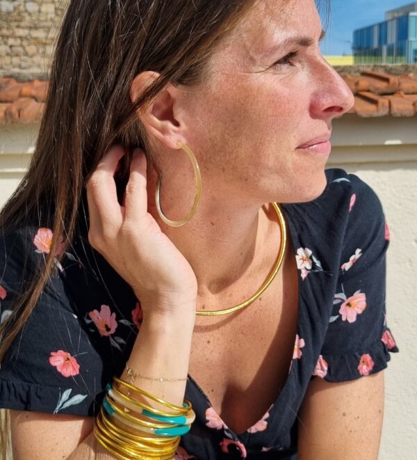 Image d’une femme portant des créoles en corne et plusieurs bracelets joncs dorés et colorés, ajoutant une touche élégante et sophistiquée à son look. Parfait pour les accessoires de mode tendance.