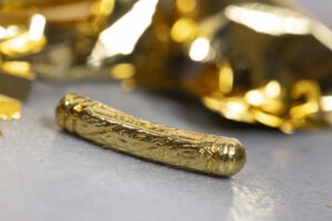 Petit cylindre en or finement gravé, posé sur une surface grise, avec un fond flou doré