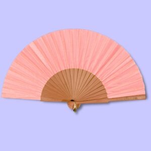 Éventail corail uni, accroché avec une attache dorée, posé sur un fond violet clair.
