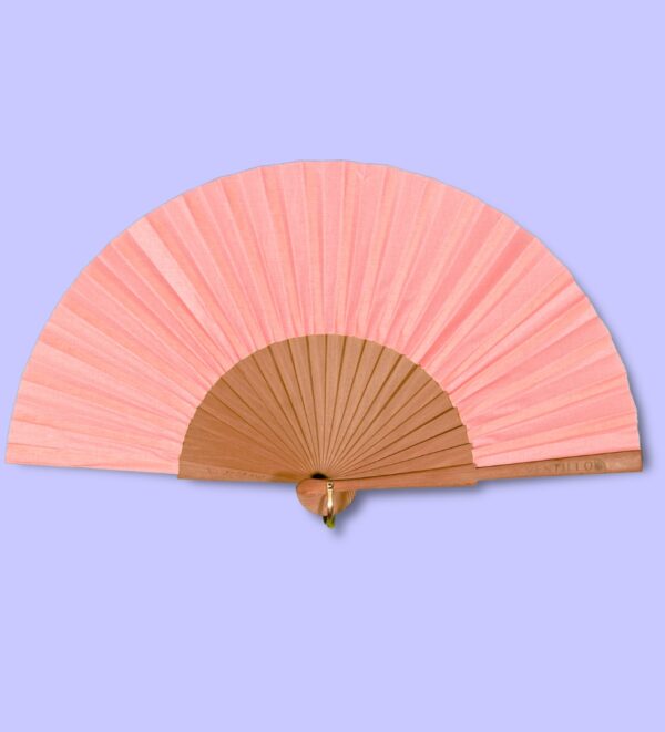 Éventail corail uni, accroché avec une attache dorée, posé sur un fond violet clair.